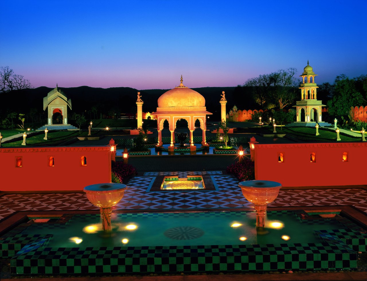 The Oberoi Rajvilas Jaipur illuminated at night with the dedicated Rajasthani fort-and-haveli architectural vocabulary set within 32 acres of landscaped gardens, ornamental pools, and the restored 280-year-old Shiva temple